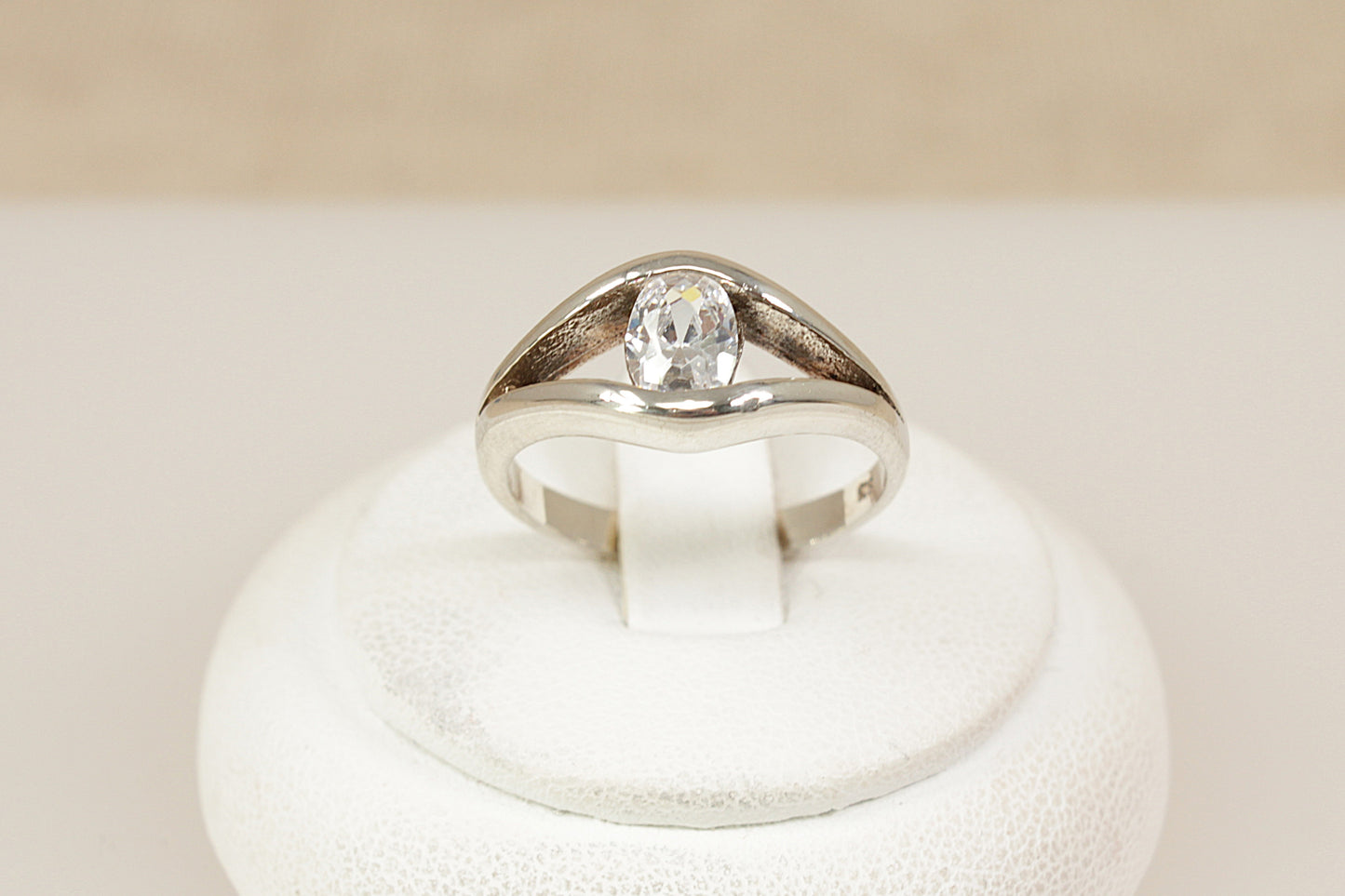 Silver solitaire ring with a cubic zirconia gemstone on a white stand against a beige background