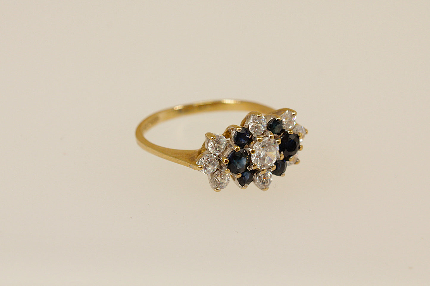 Gold ring with blue and white gemstones on a beige background