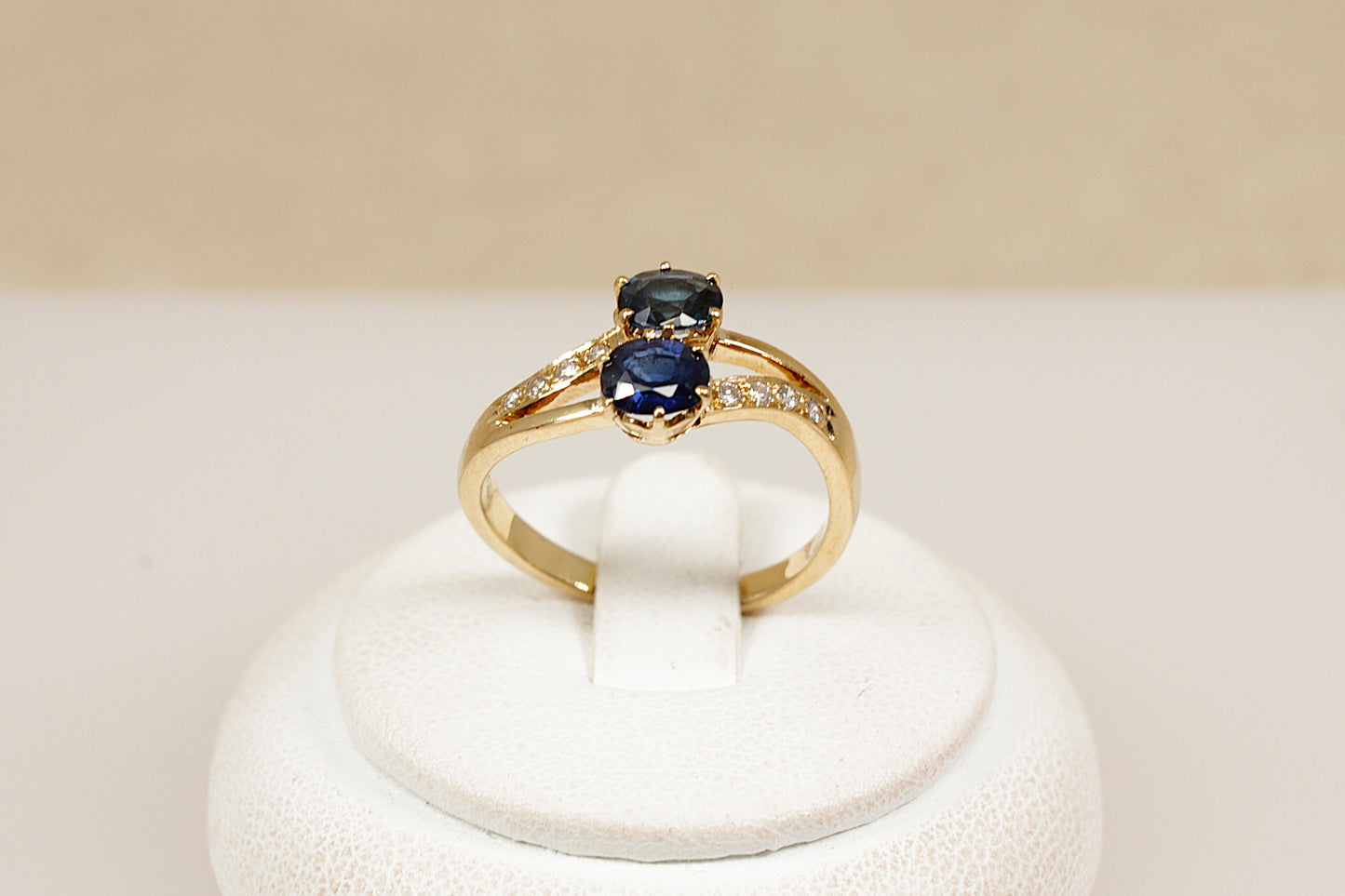 A timeless and romantic design, this 18ct gold ‘Duo’ ring features two round-cut midnight blue sapphires, securely claw-set side by side in a crown-style, split-head setting. The sapphires are positioned on a subtle twist, Each shoulder is adorned with four sparkling diamond accents, adding delicate brilliance and enhancing the ring’s refined elegance. The band is stamped ‘750’ for 18ct gold. UK finger size O.
