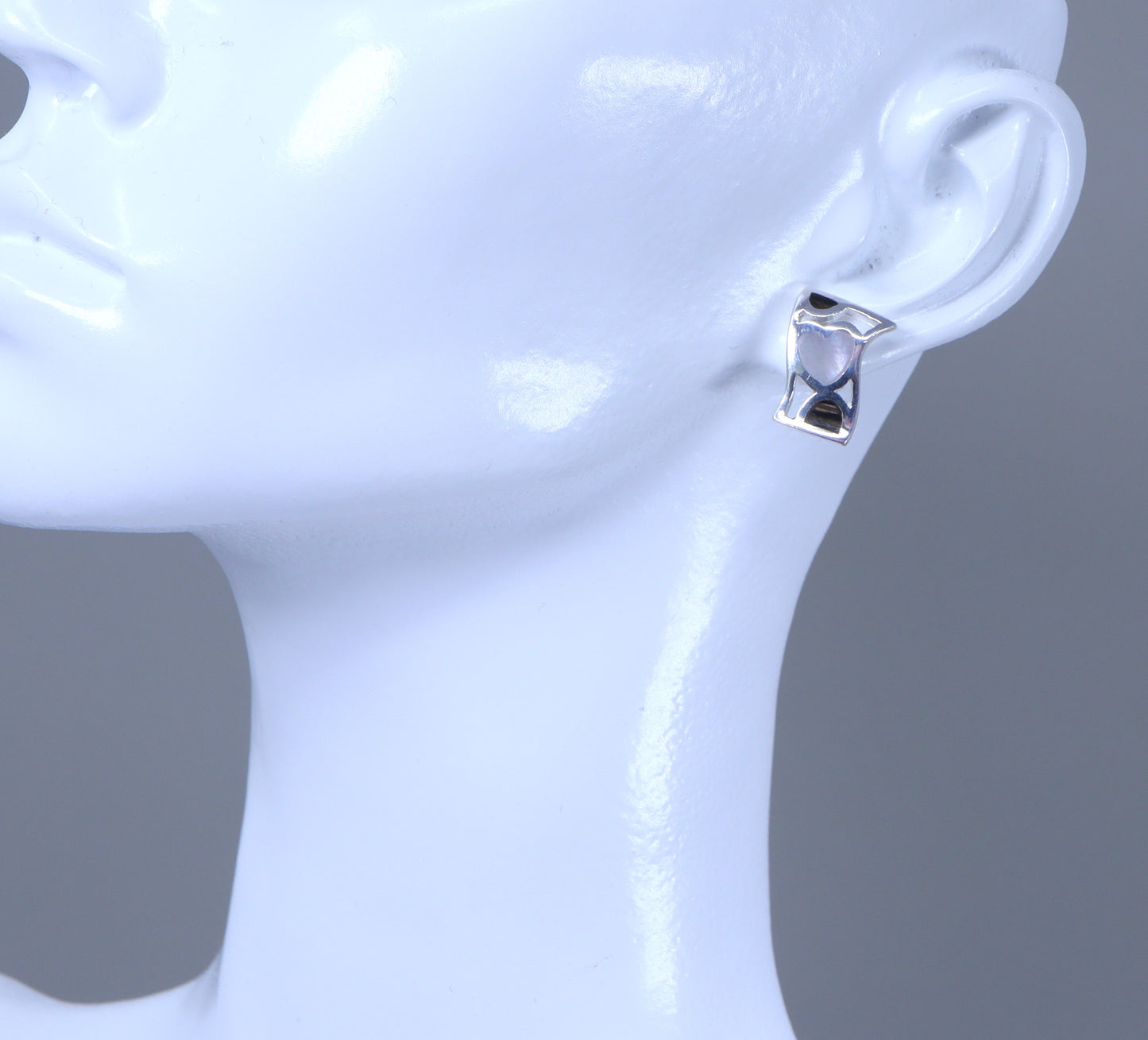 Silver earring on a mannequin ear with a plain background