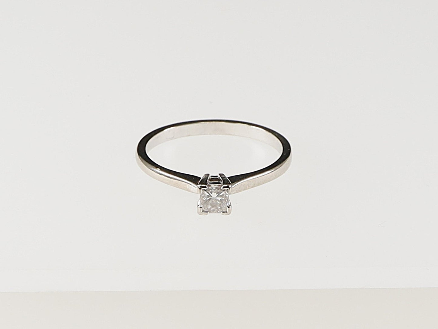 An 18ct white gold diamond solitaire ring with a princess cut diamond set in a 4 claw basket setting. This ring would make an ideal Engagement ring. It is in excellent condition and has London hallmarks on the inside of the band. UK Finger size P.