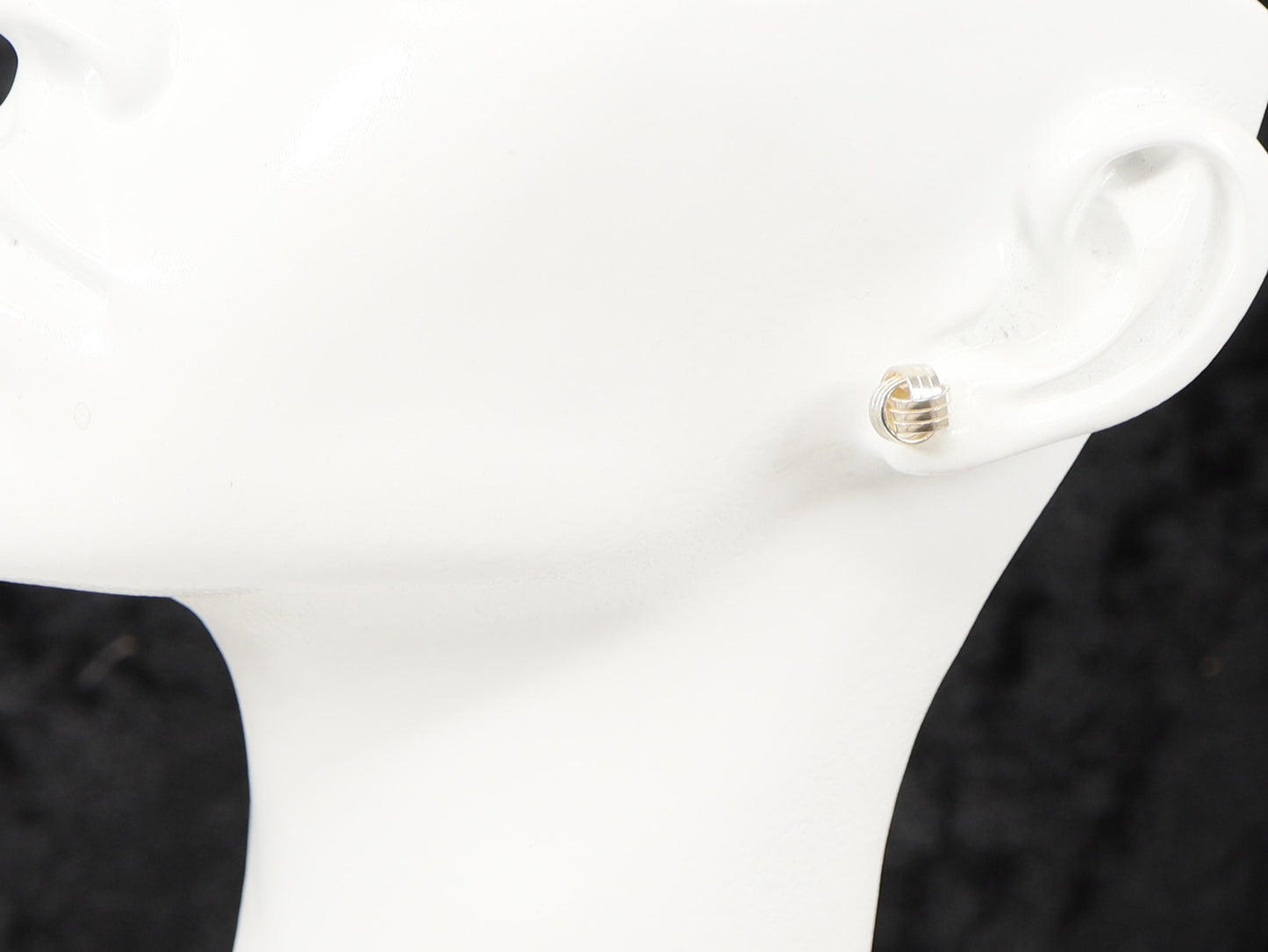 A pair of silver stud earrings with a knot design displayed on a mannequin ear.