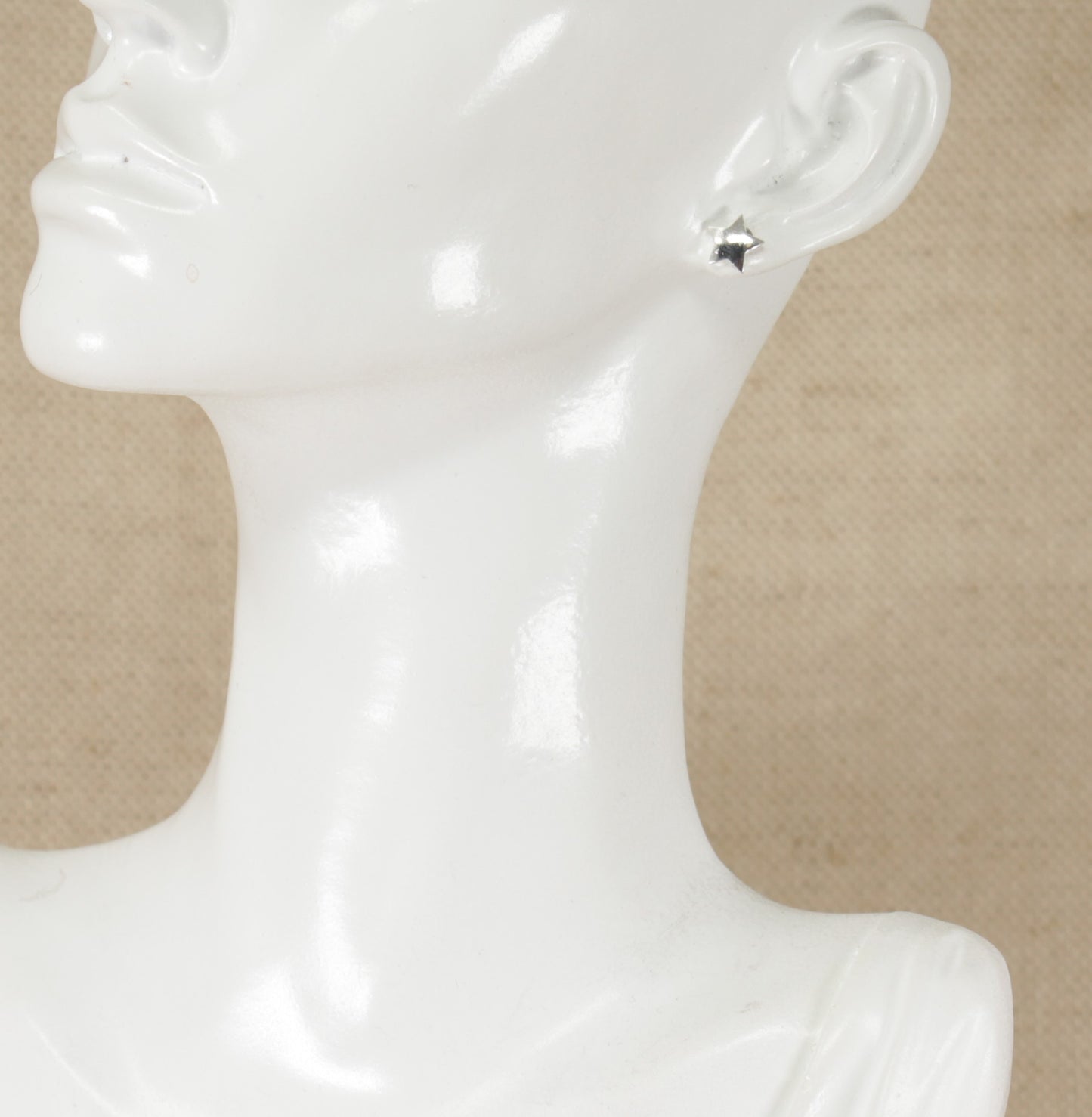 A pair of silver stud earrings in the shape of a 5 pointed star displayed on a mannequin head.