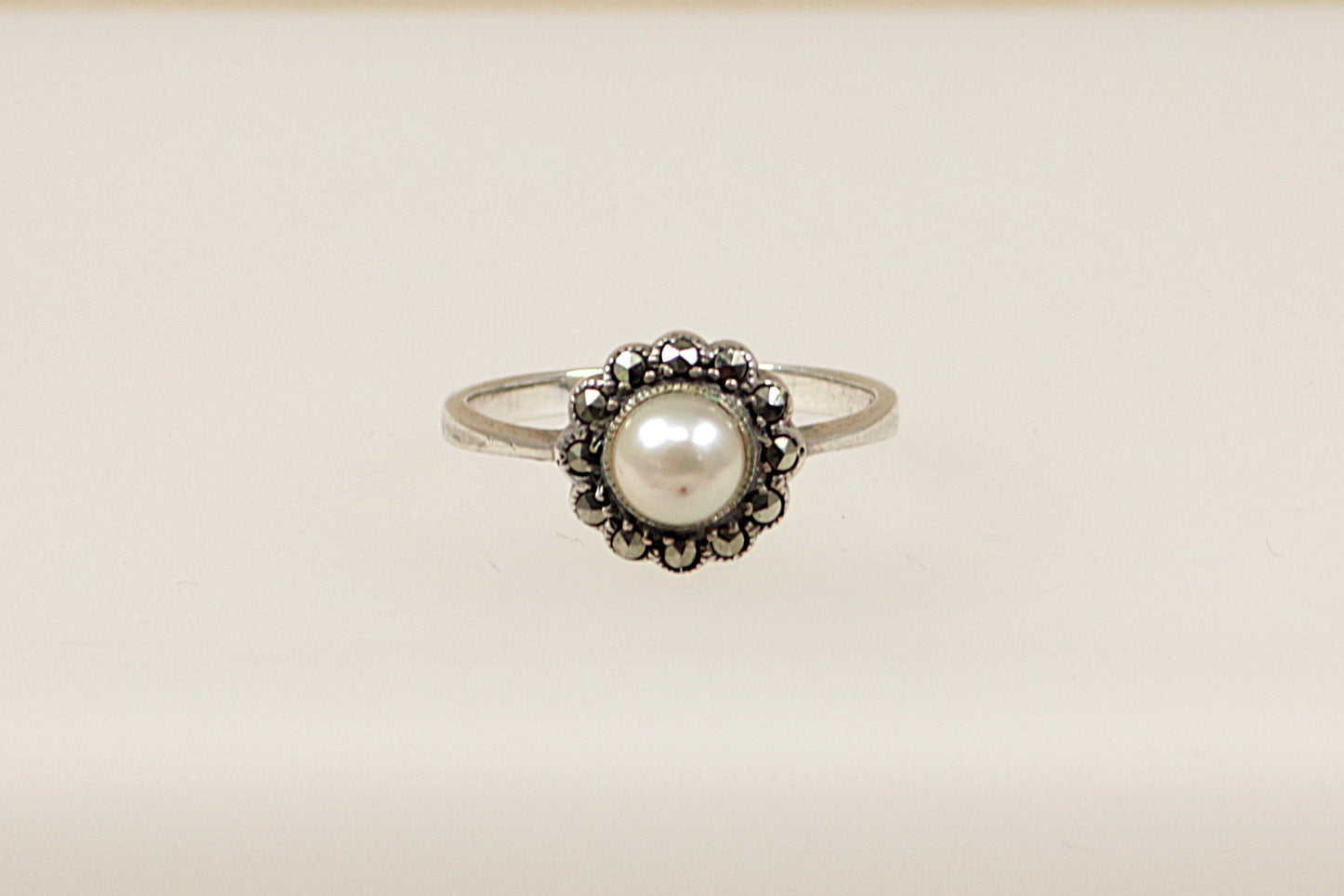 A silver ring with a central faux pearl surrounded by marcasite stones set in a circular pattern.