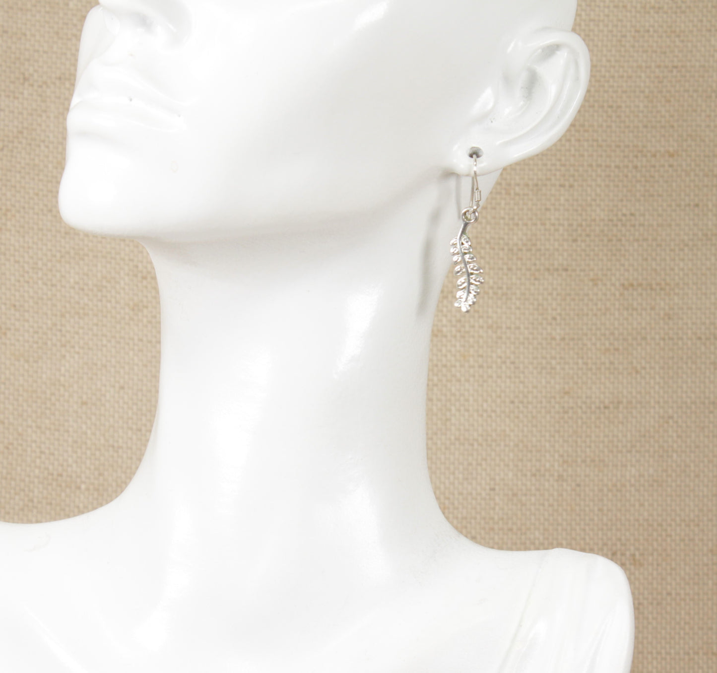 A pair of sterling silver earrings in the shape of a fern leaf on a mannequin head.