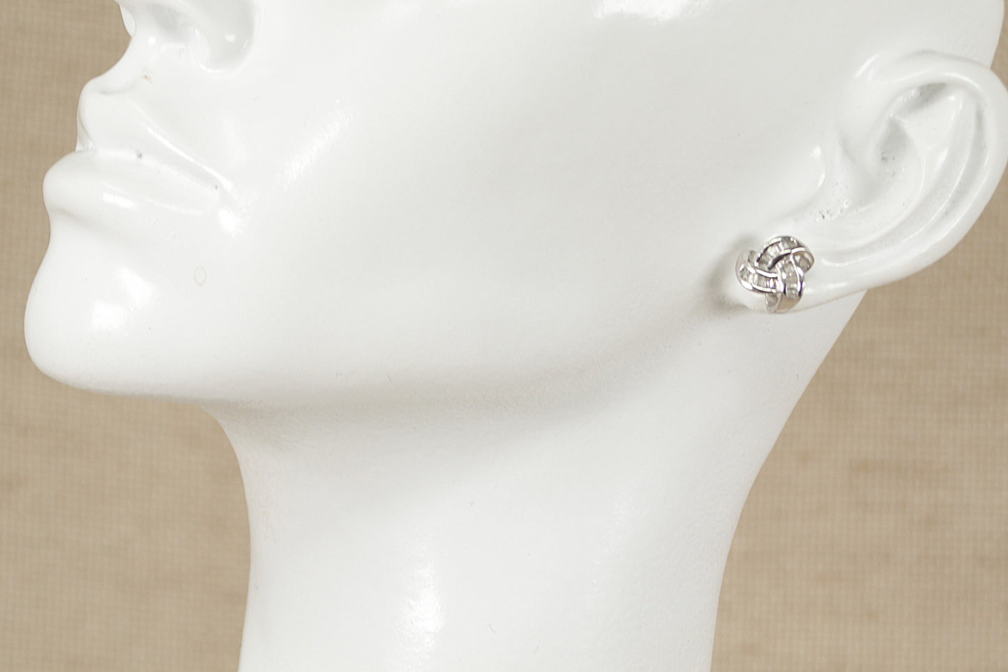 A pair of silver and cubic zirconia knot design stud earrings displayed on a mannequin head.