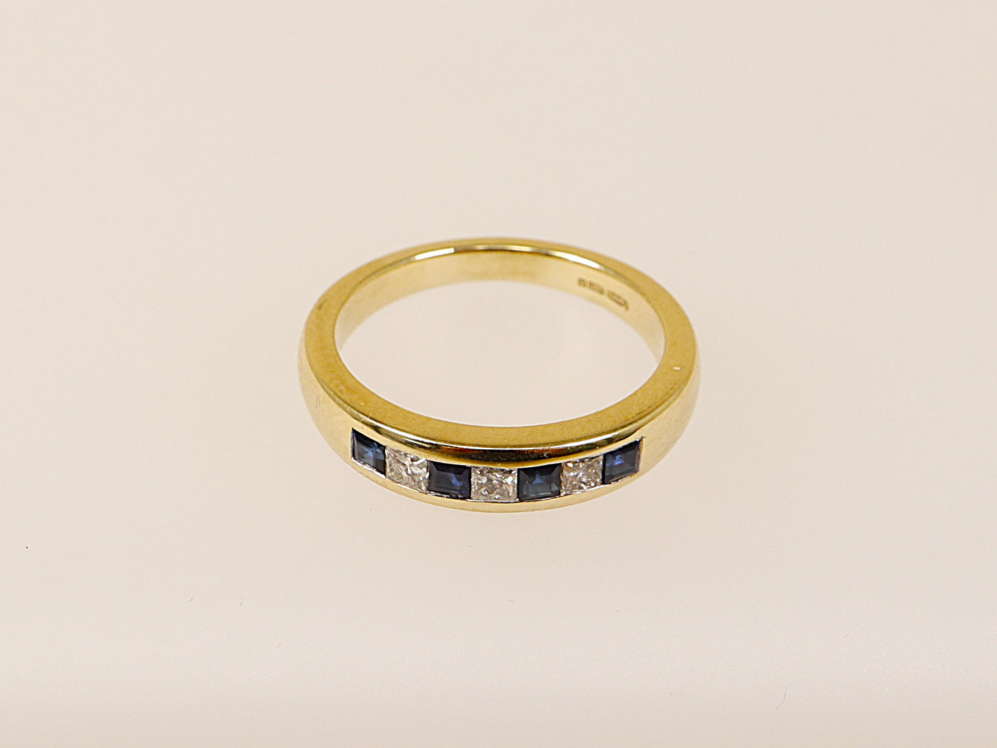 A 9ct gold band ring with channel-set blue sapphires and princess-cut diamonds