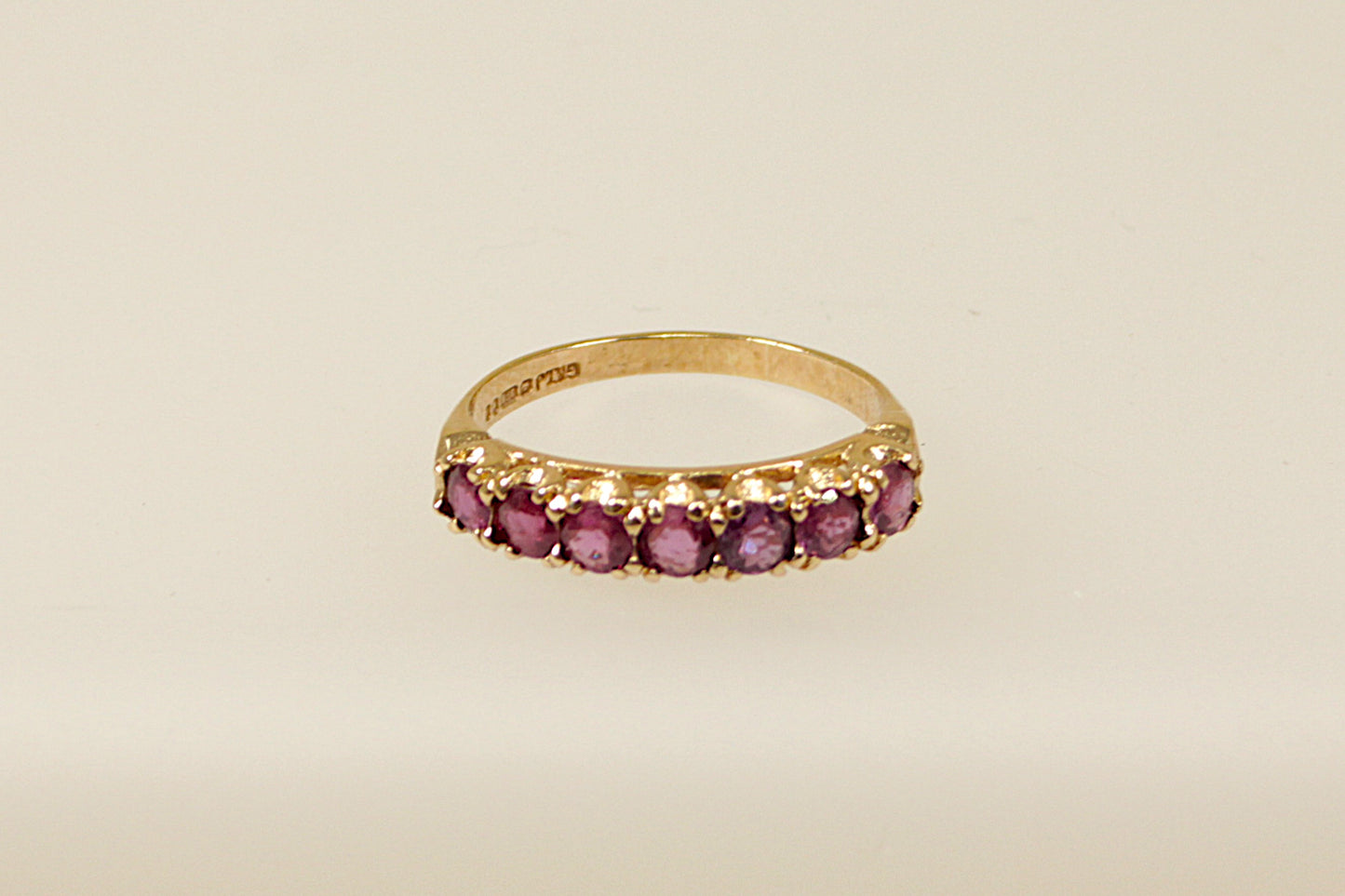 A vintage 9ct gold half eternity ring with seven claw set pink topaz gemstones on a white background.