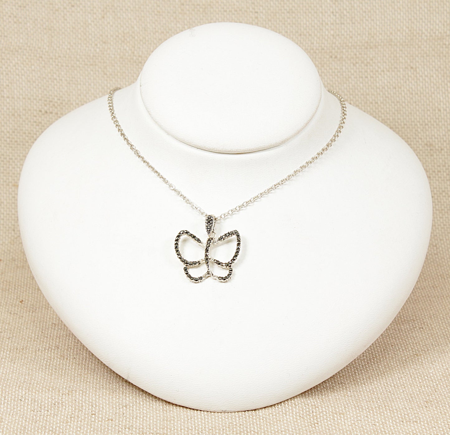 A silver butterfly pendant necklace with marcasite stones on the edges displayed on a white mannequin.