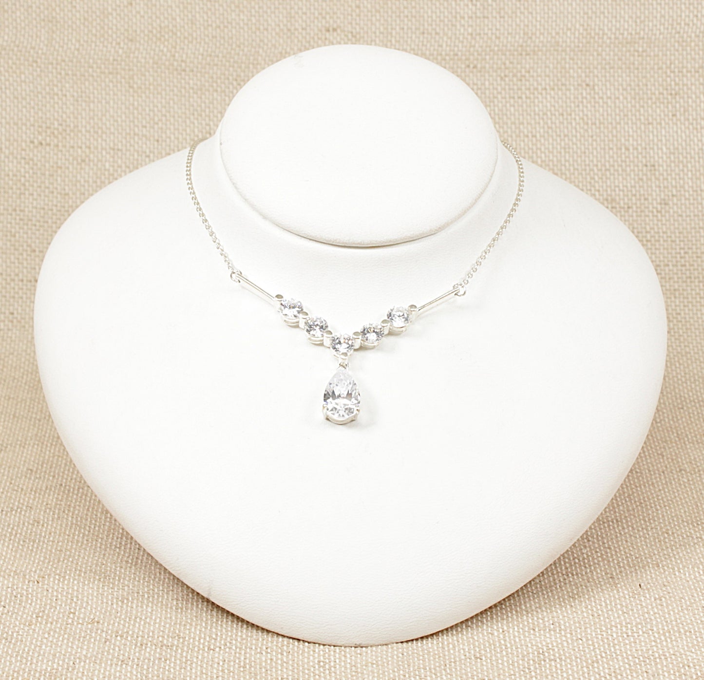This silver necklet features an elegant arrangement of cubic zirconia gemstones, creating a sparkling and sophisticated look. The design includes five round CZ stones set along a V-shaped mount, which adds a graceful contour to the necklace. The V shape not only accentuates the neckline but also gives a modern and refined touch to the piece. The necklet is in excellent condition and stamped 925 for sterling silver.