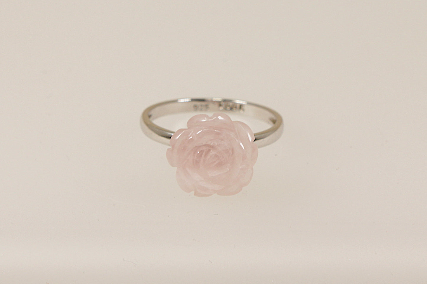 A silver ring with a carved pink rose as the central stone, displayed against a white background.