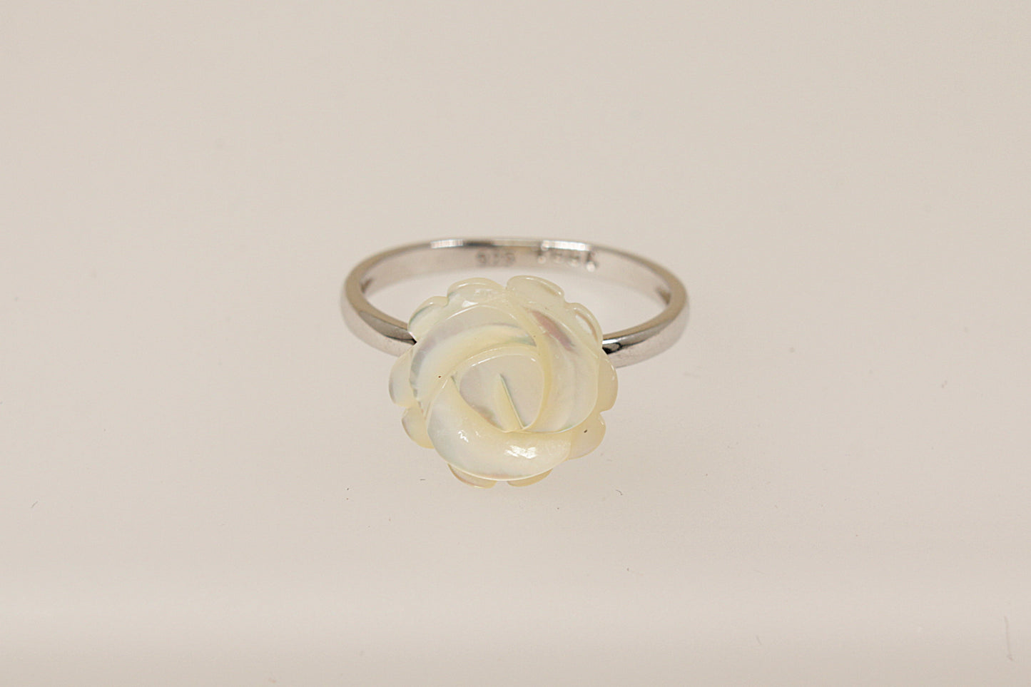 A silver ring with a carved white mother of pearl rose in full bloom on a white background.