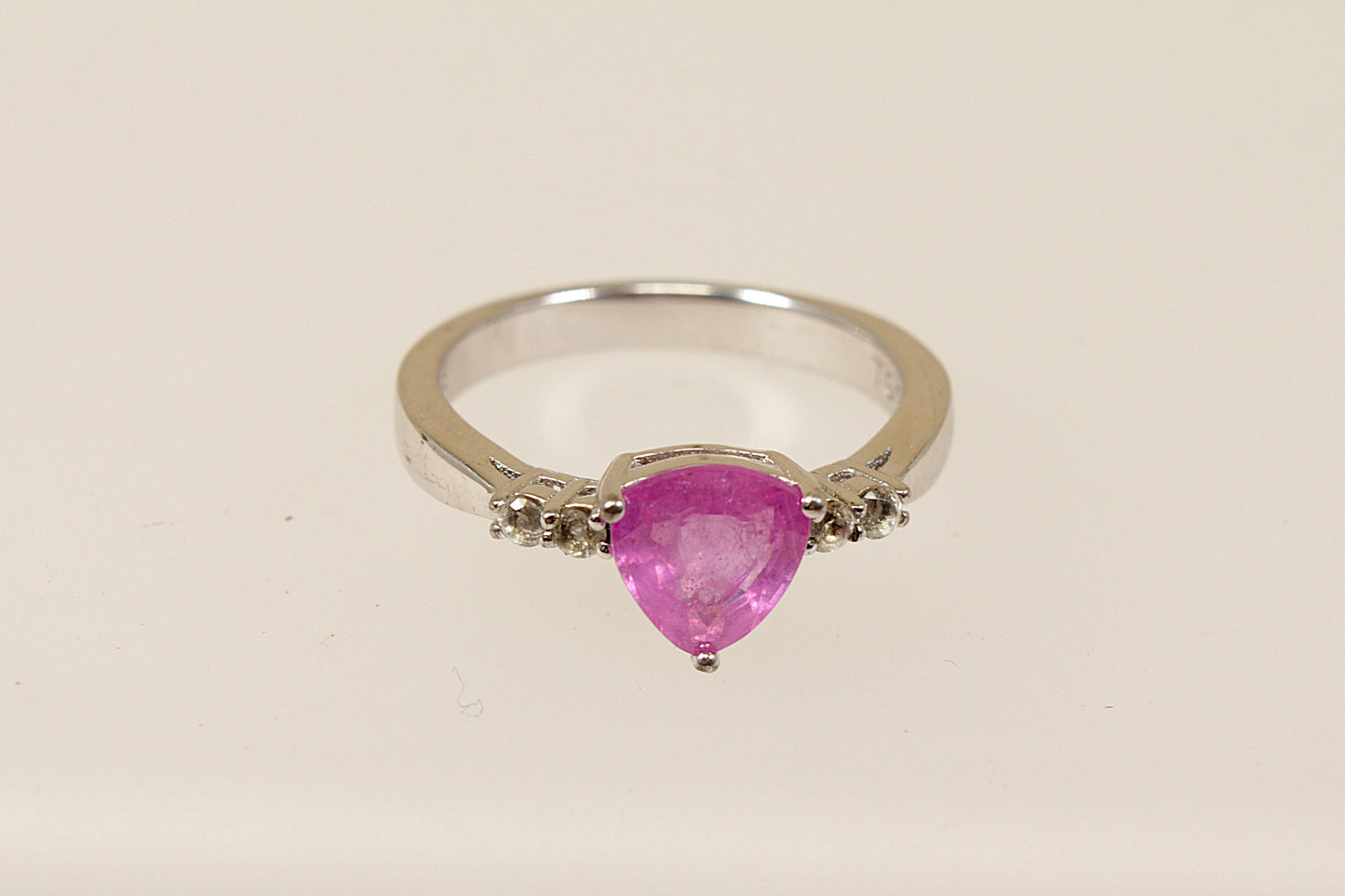 A sterling silver trillion cut pink sapphire solitaire ring with white topaz accents, Stamped 925 for sterling silver and the makers mark ‘TGGC’ for The Genuine Gemstone Company, UK finger size O.