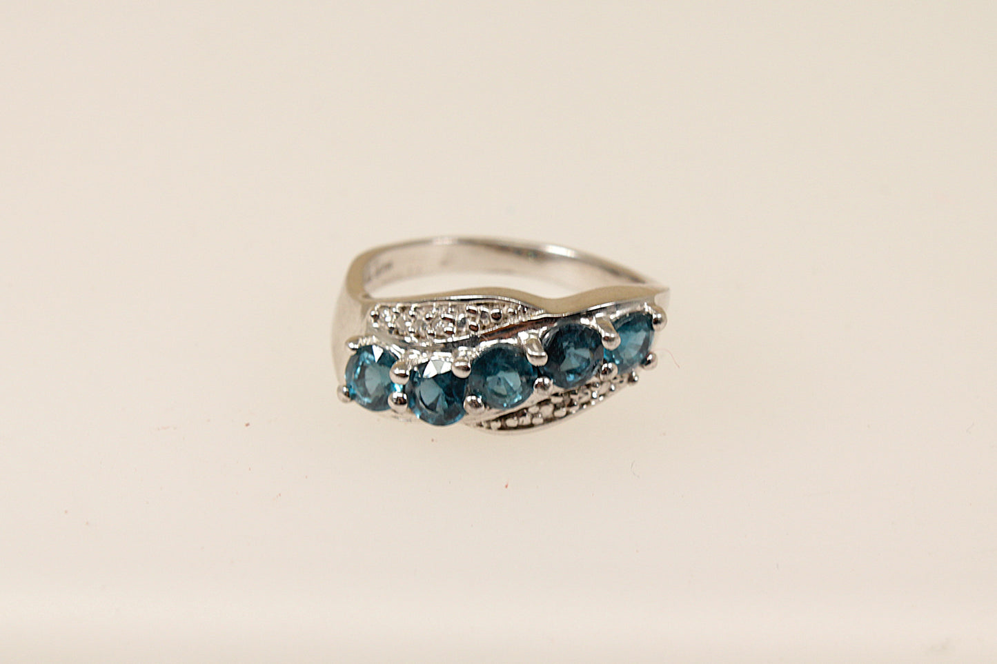 A sterling silver ring with five round blue topaz gemstones set across the band in a graceful curve with claw settings.