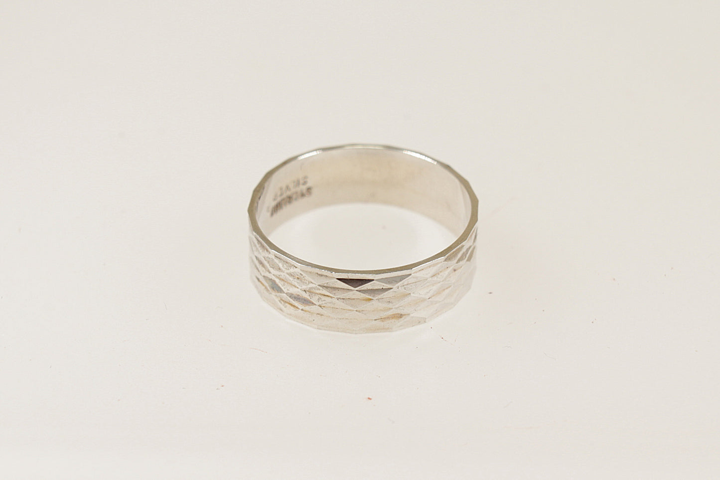 A silver band ring with an engine turned pattern, displayed against a white background.