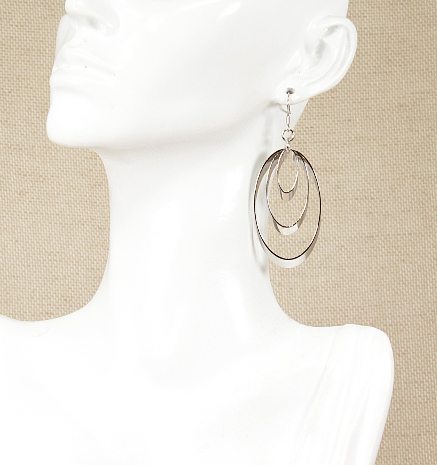 A pair of silver drop earrings with a trio of oblong rings on a mannequin head.