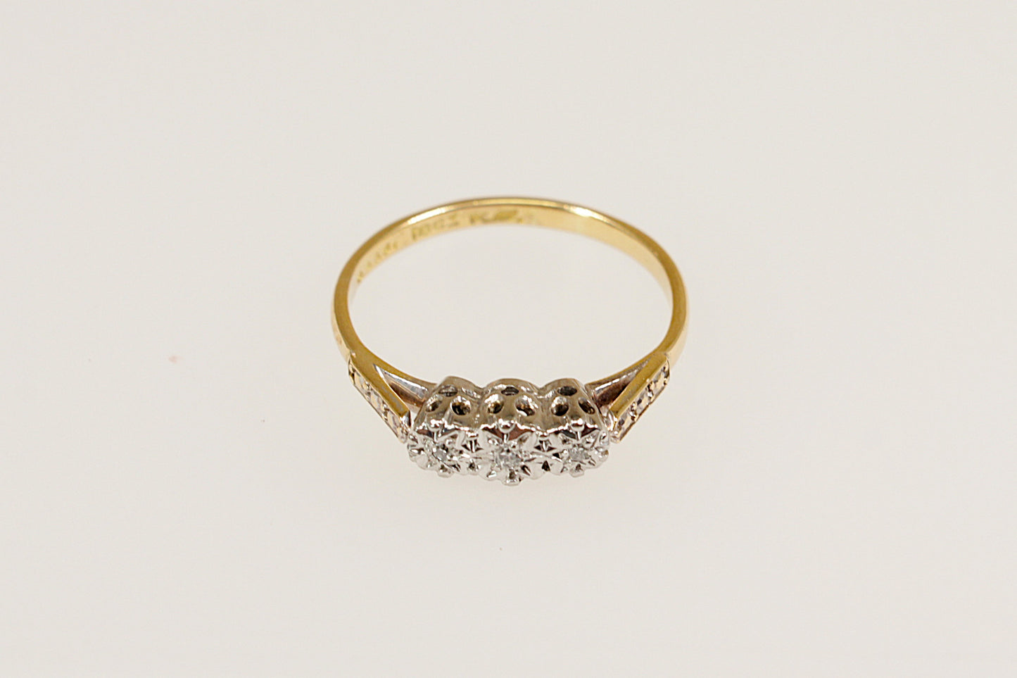An 18ct Gold and Platinum Diamond Trilogy Ring with a central larger diamond flanked by two smaller diamonds on each side, set against a white background.
