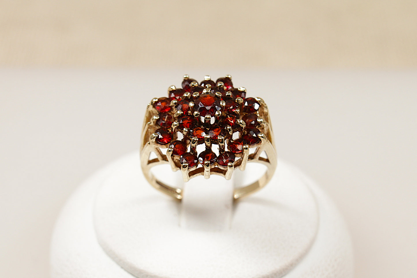 A 9ct gold garnet cluster ring with multiple garnet stones arranged in a circular pattern in the center, displayed on a white mount.