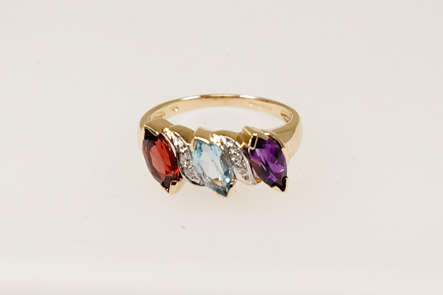 This pretty and unique piece of jewellery is handcrafted in 9ct Gold and features 3 Marquis cut gems that are interspaced with Diamond accents. The gemstones are Garnet, Blue Topaz and Amethyst, these are arranged on a slant, creating a dynamic, stylish appearance. There are 4 diamond accents enhancing the rings sparkle and sophistication. UK finger size O.