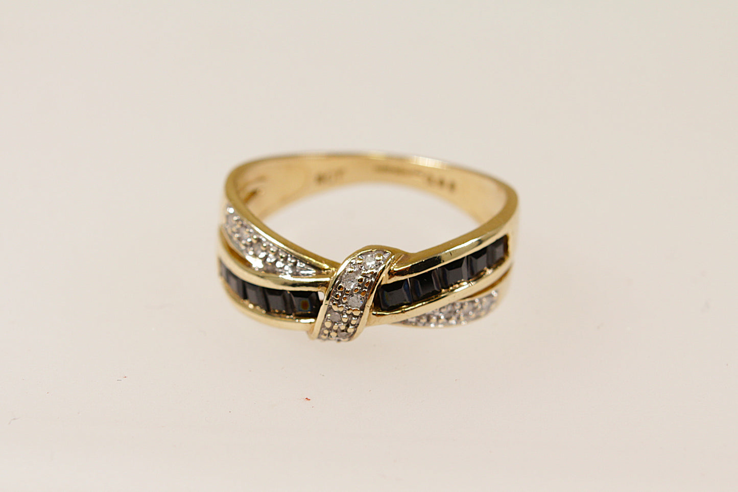 A 9ct gold ring with a bow design, featuring channel set blue sapphires along the loops and claw set round diamonds along the ribbon, displayed against a white background.