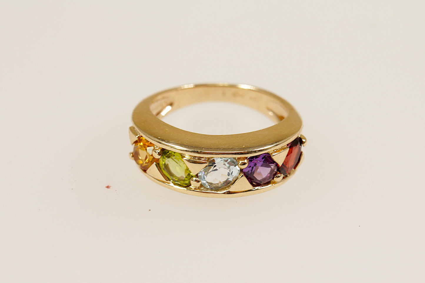 A 9ct gold ring with multiple oval gemstones set in a line on the top, including citrine, peridot, white topaz, garnet, and amethyst. UK finger size M.