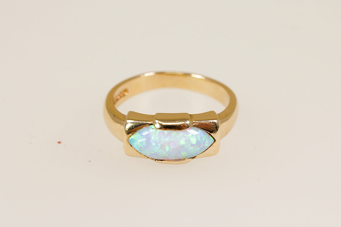 A 9ct gold ring with an opal centerpiece set in a rectangular bezel, displaying vibrant orange, red, and yellow hues against a white background. UK finger size O.