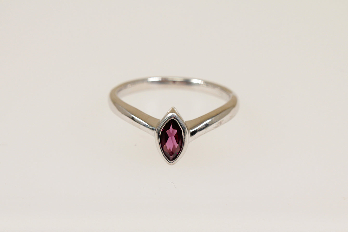 A marquise cut garnet ring with a bezel setting, in silver color, with a white background.