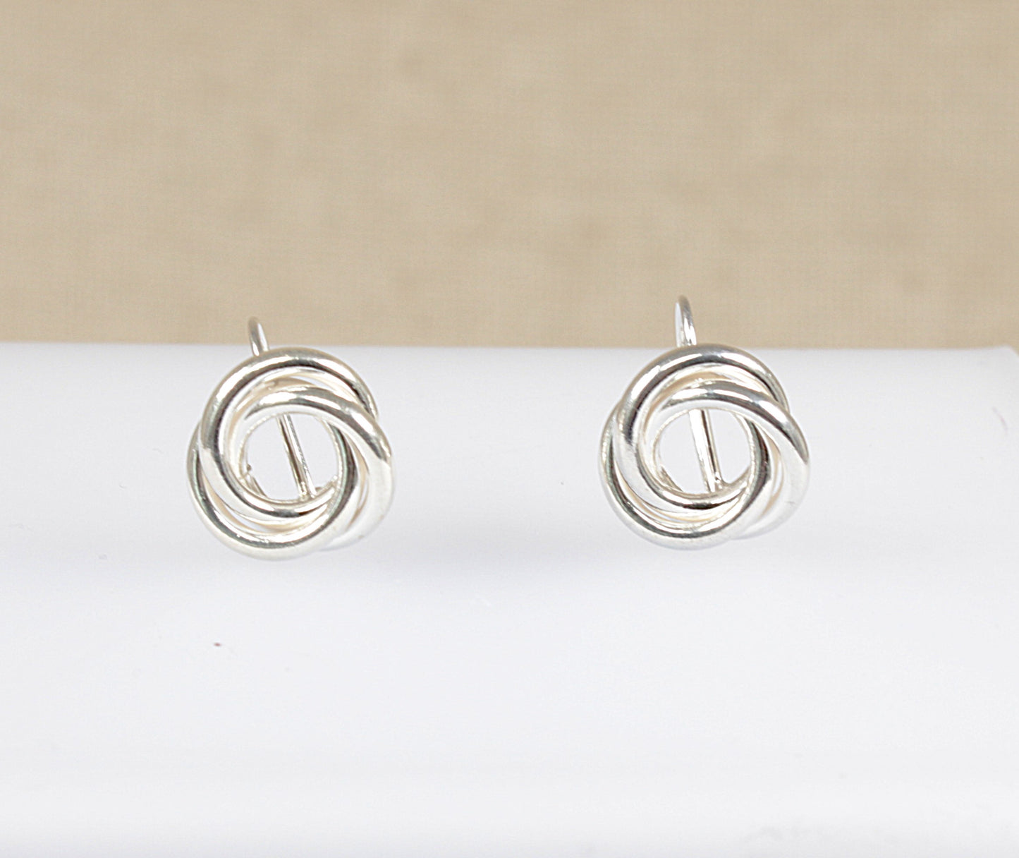 A pair of silver earrings with a round interlocking swirl design displayed against a beige background.