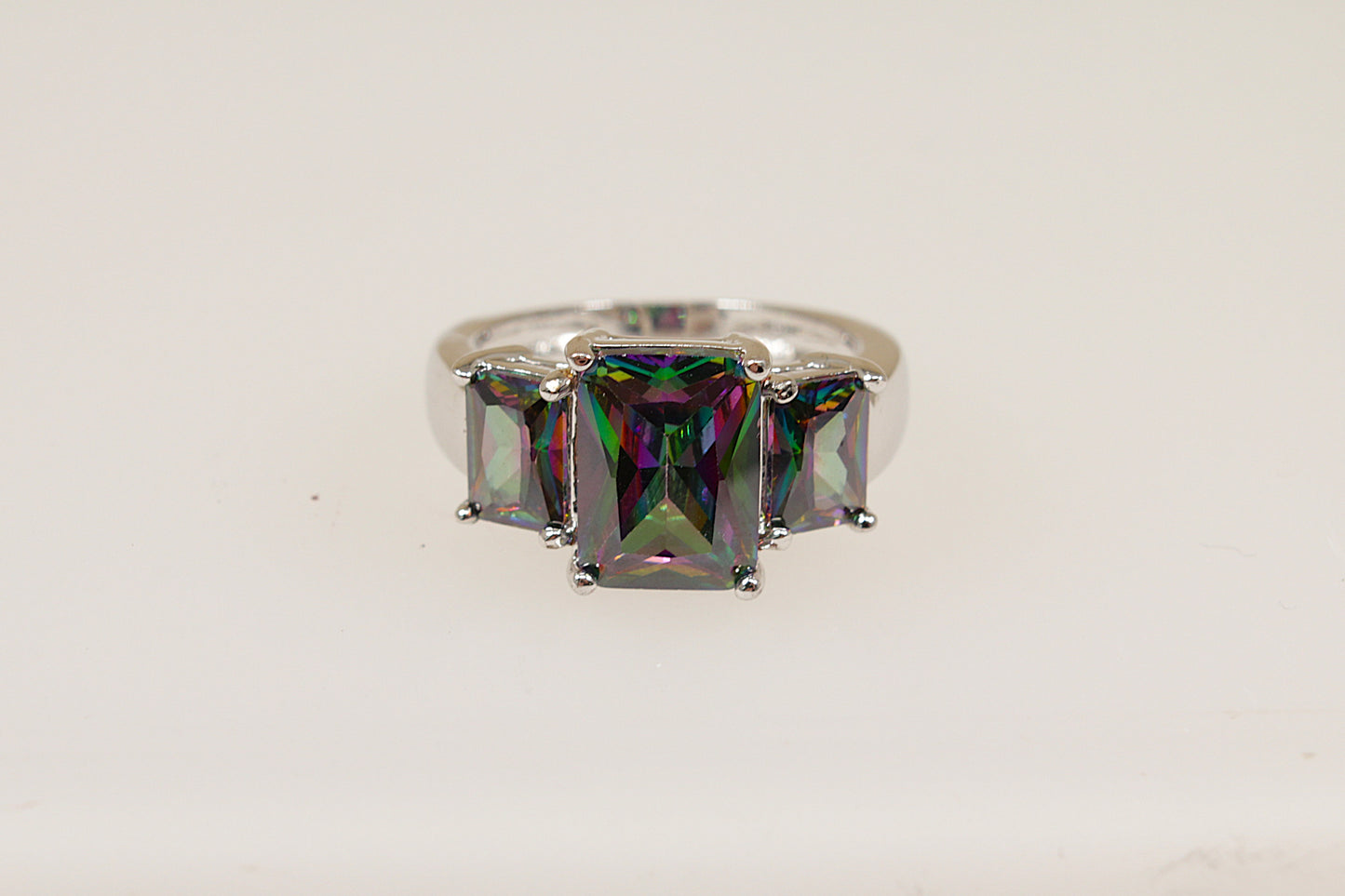 An elegant sterling silver ring with a central emerald cut mystic crystal gemstone, flanked by two smaller side stones, set in a crown setting.