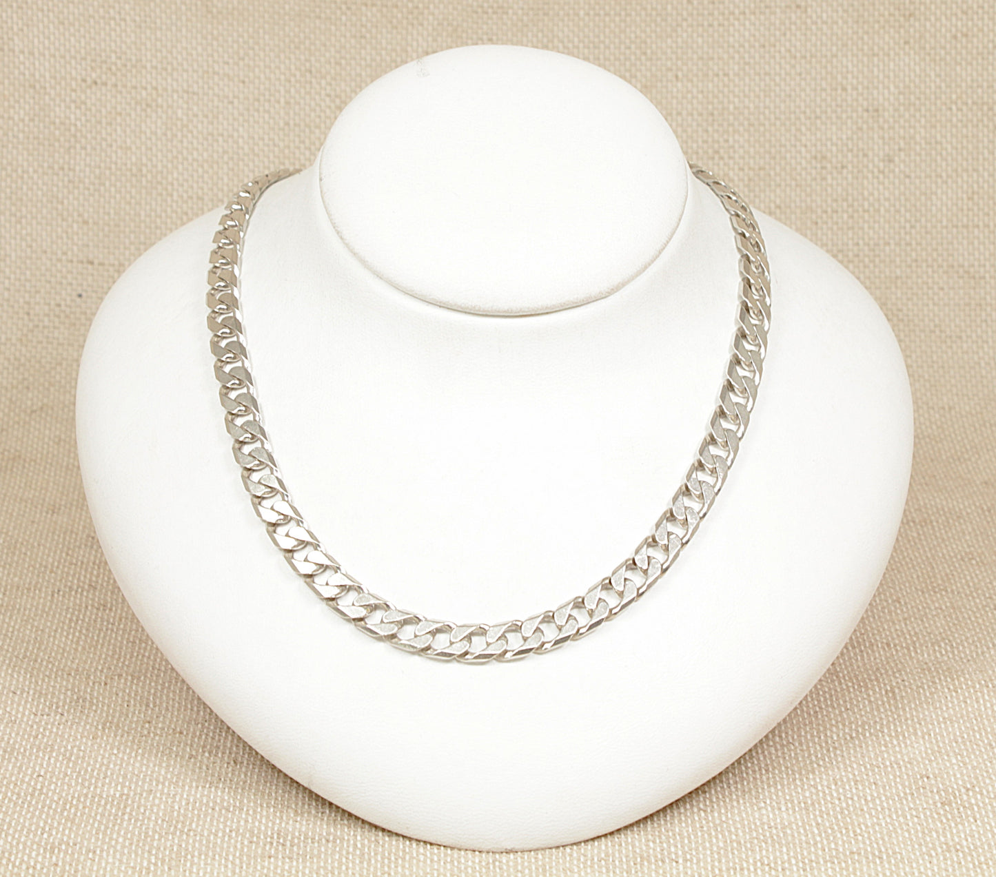 A silver curb link necklace displayed on a white mannequin bust against a beige background.