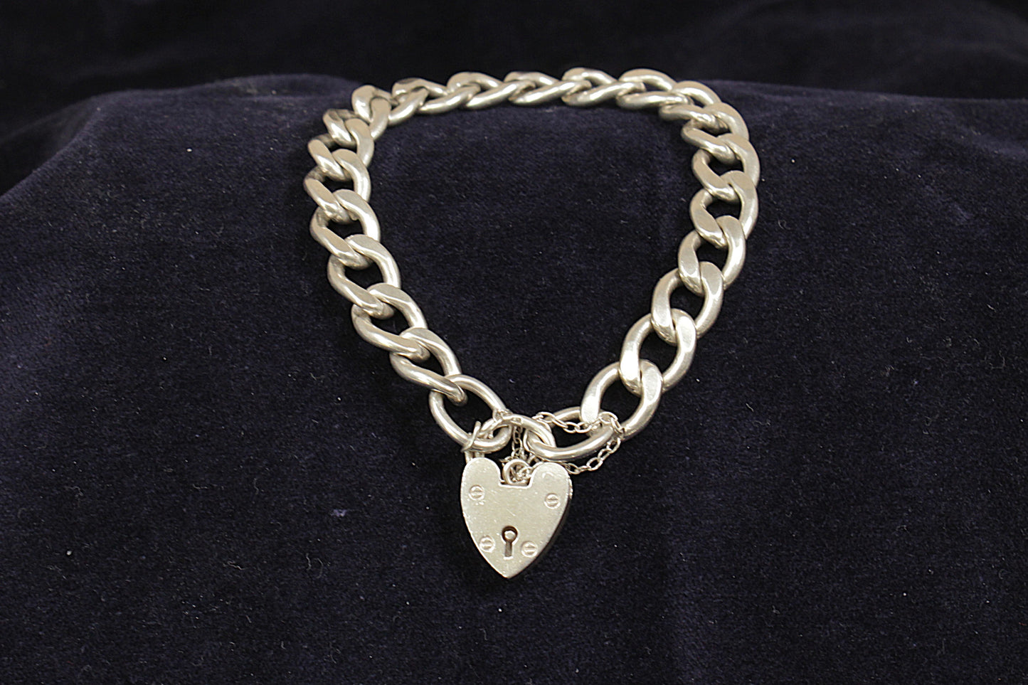A vintage silver curb link bracelet with a padlock fastening and a safety chain, displayed on a black background.