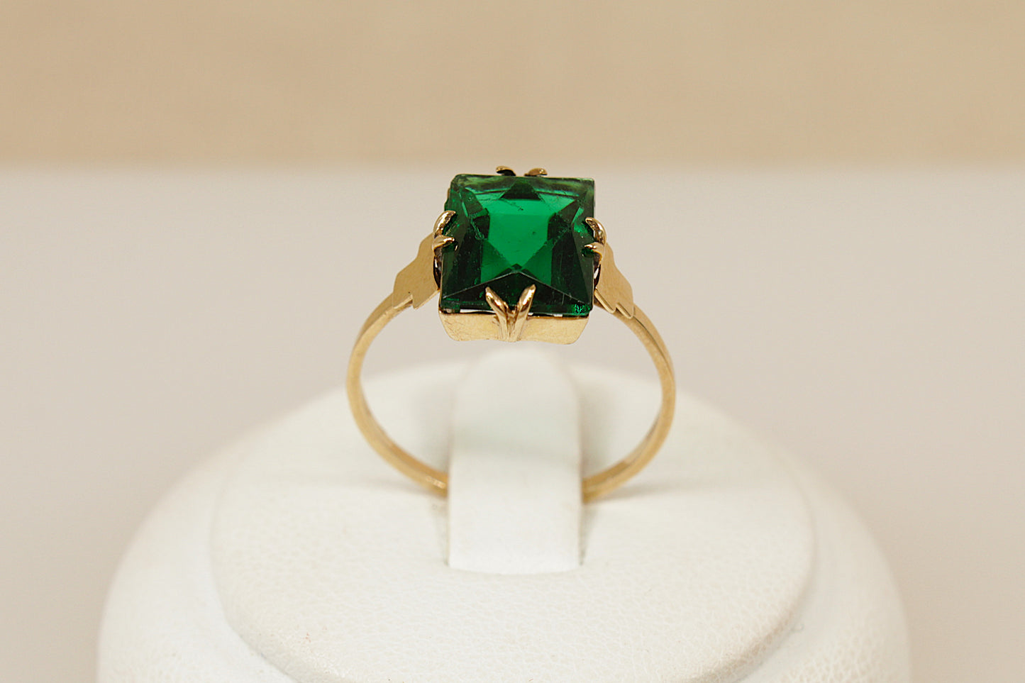 Art Deco Vintage Gold ring with a green gemstone on a white stand against a beige background