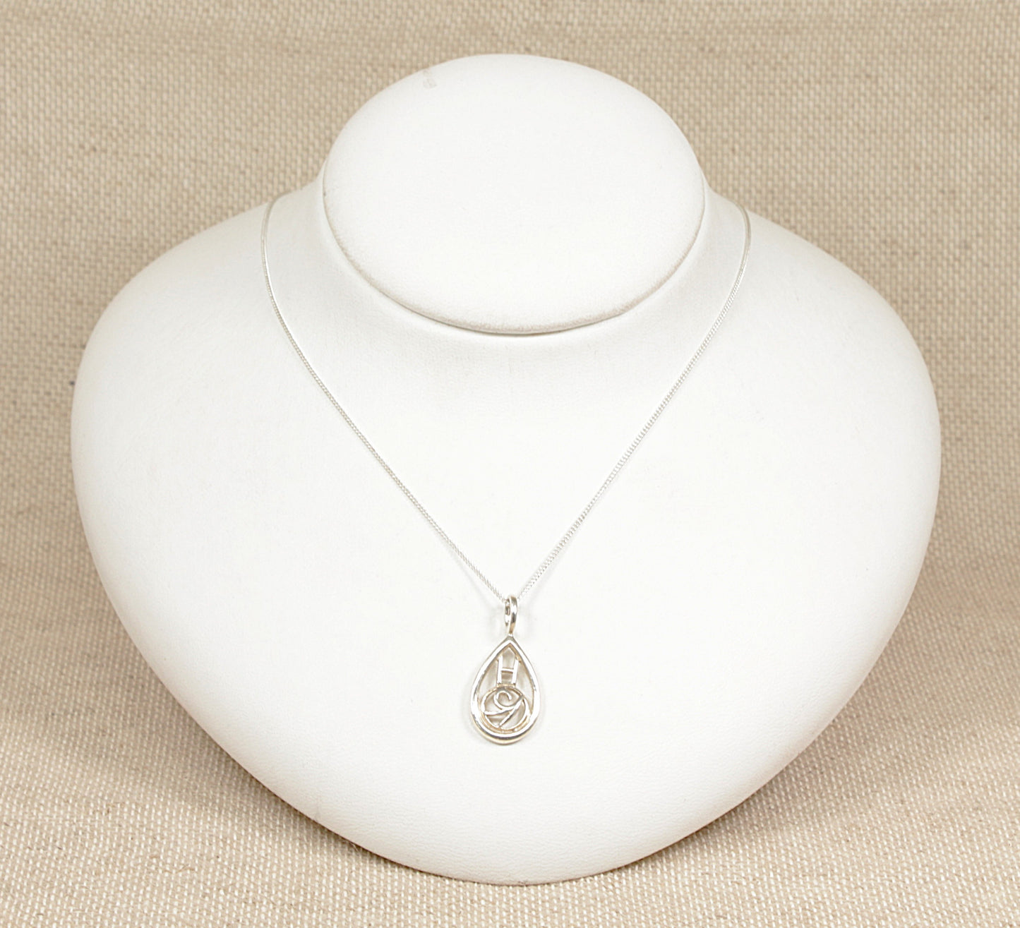 A sterling silver pendant necklace with a teardrop shape featuring a floral and rectangular design on an 18 inch curb chain, displayed on a white mannequin.
