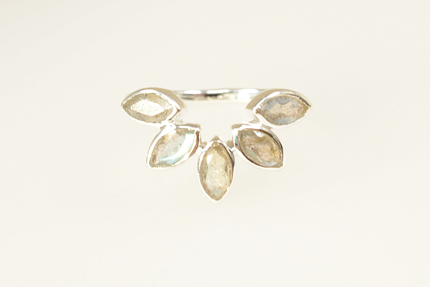 This Silver designer ring has a stunning and unique design. Handcrafted by the designers at POM 925, it has 5 marquis cut Labradorite gems, bezel set, that’s arranged in a half-halo flower pattern.
The marquis cut stones emphasise the natural flash of labradorescence and the bezel settings provide both security and a sleek modern look. It is stamped 925 inside the band for sterling silver. UK finger size P.