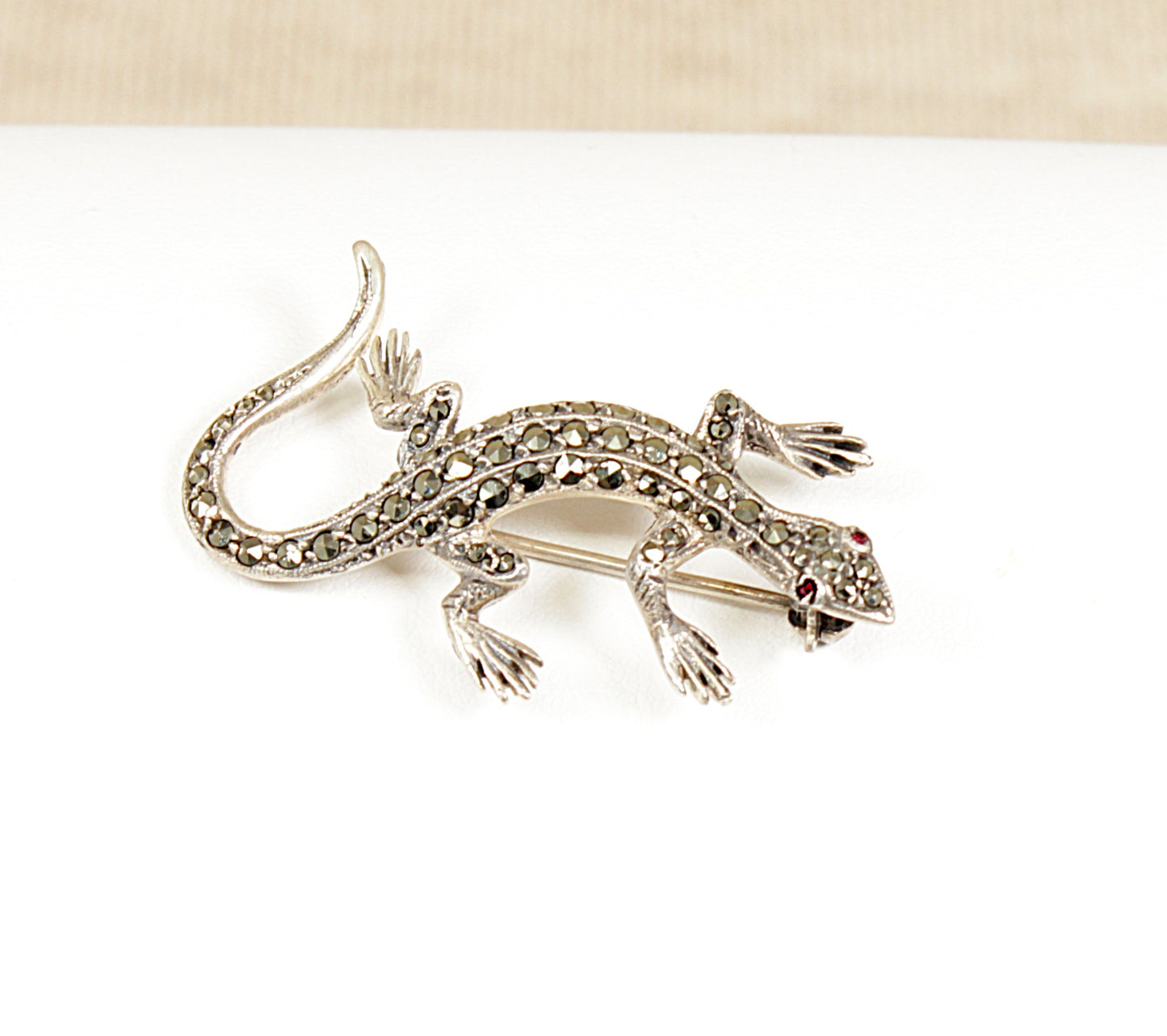 A vintage silver brooch in the shape of a gecko with marcasite stones and ruby-coloured eyes.