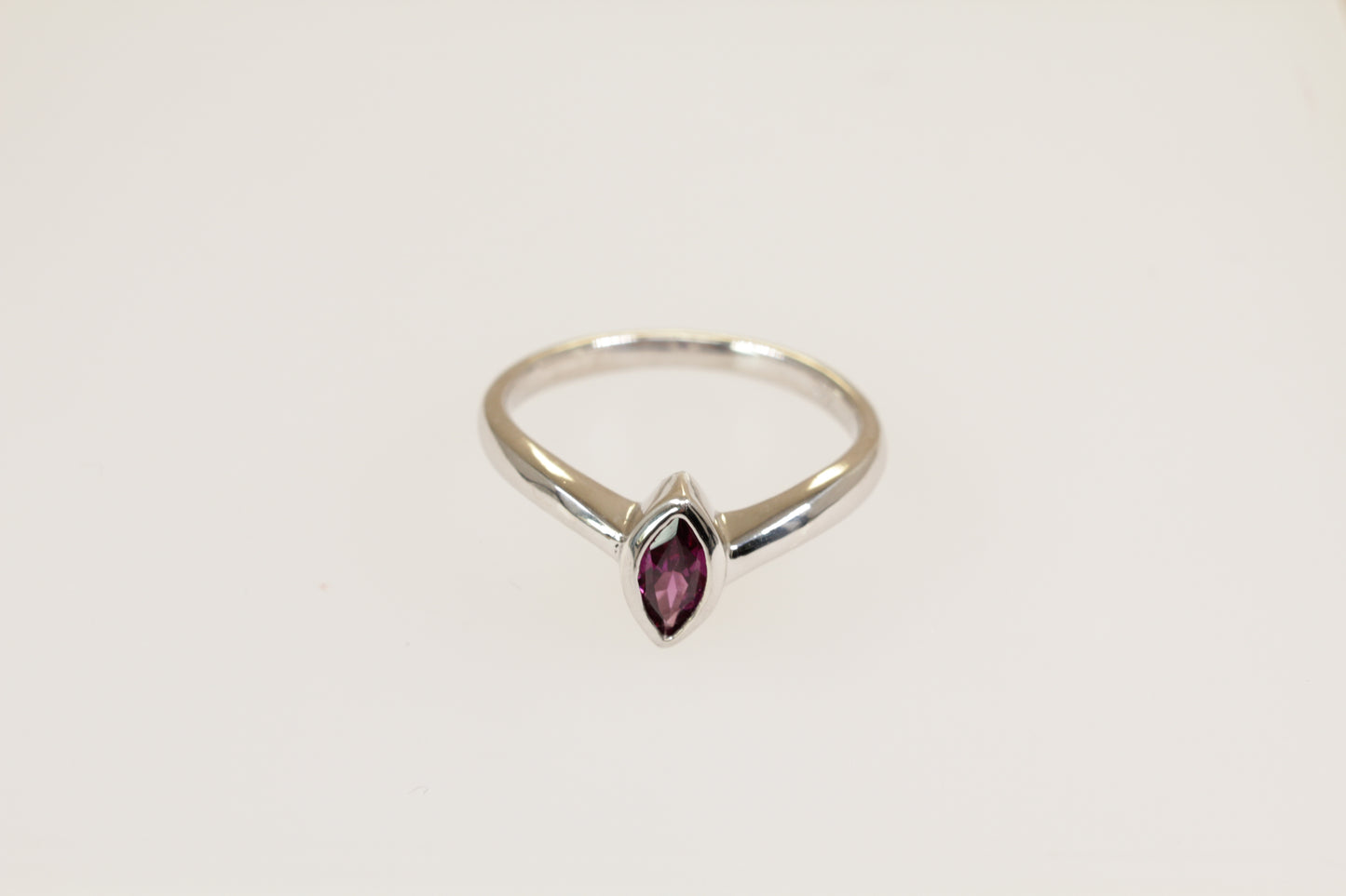 A silver solitaire ring with a marquise cut garnet in a bezel setting, on a plain white background.