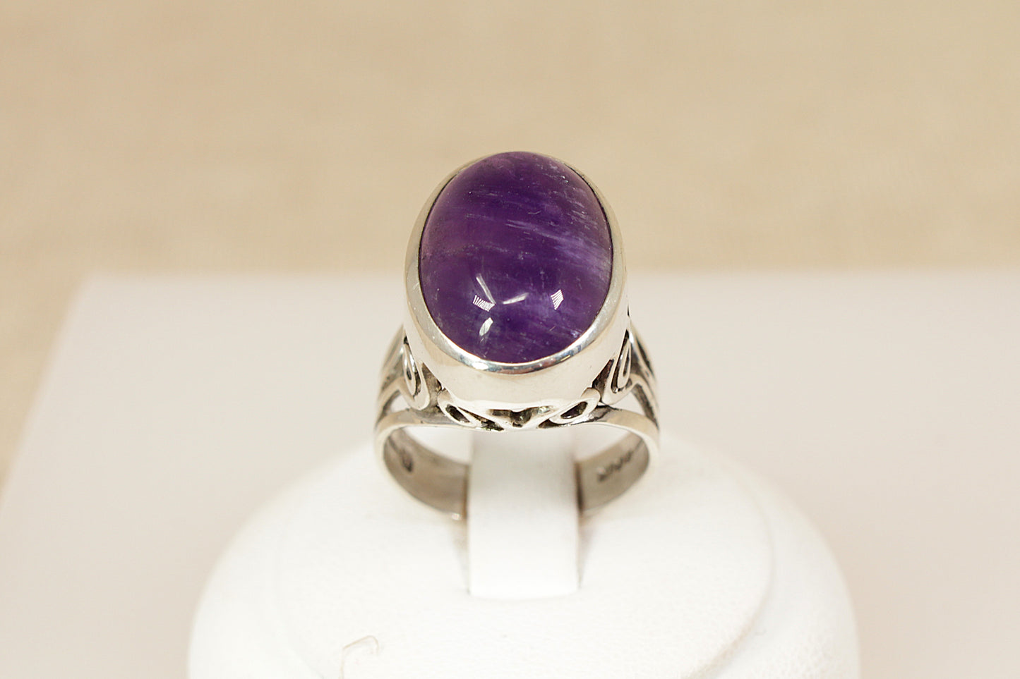 Silver ring with a purple gemstone on a white stand against a beige background