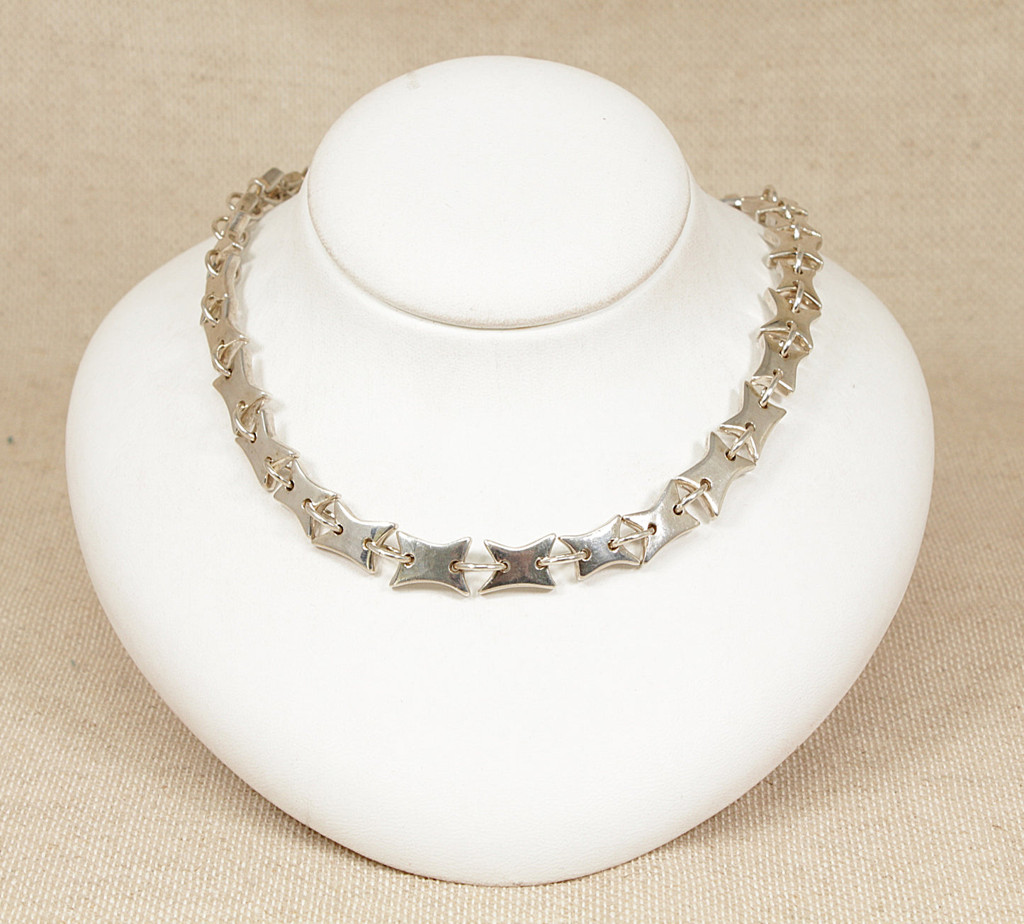 Silver necklace on a white mannequin bust against a beige background
