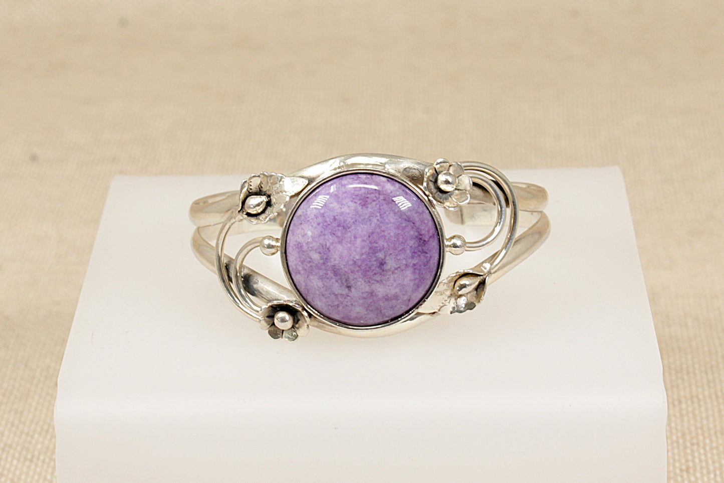 Silver bracelet with a Amethyst gemstone on a white stand against a beige background