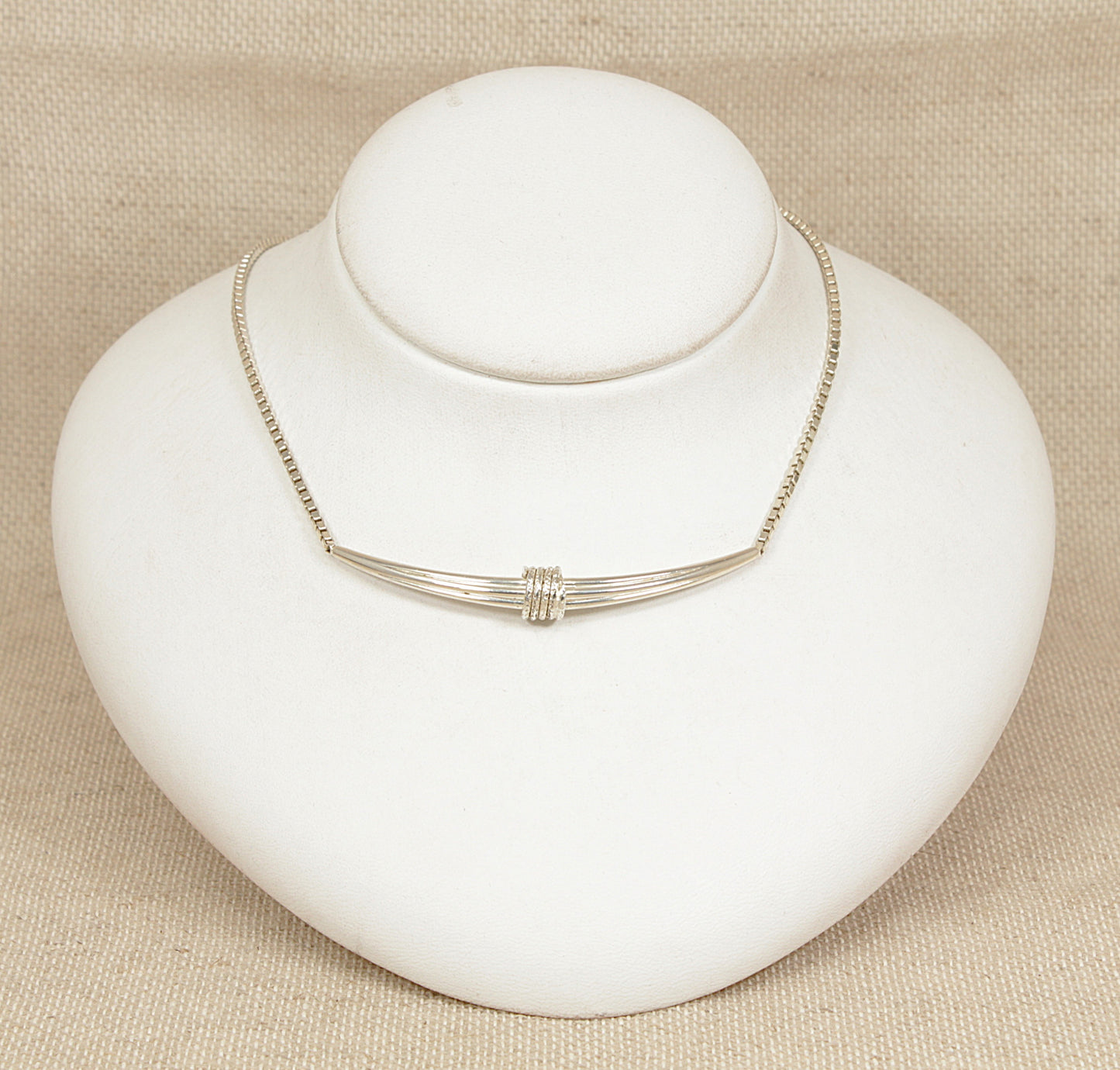 Silver necklace on a white mannequin bust against a beige background