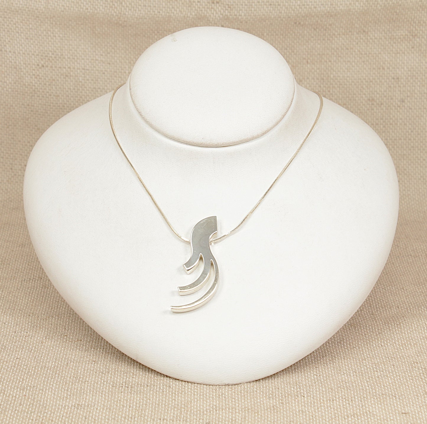 Silver necklace with a unique pendant on a white stand against a beige background