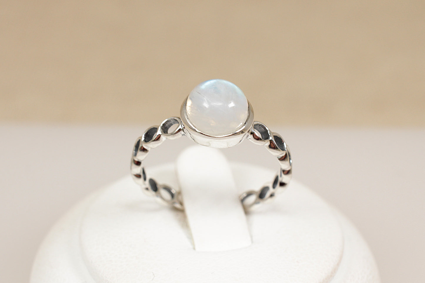Silver ring with a round gemstone on a white stand against a beige background