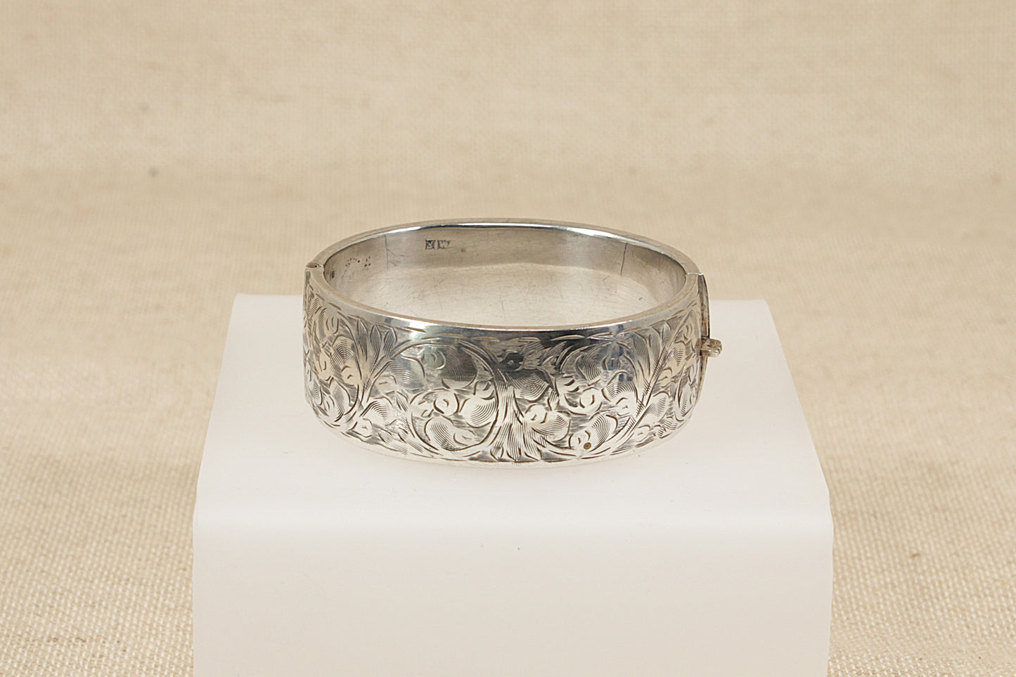 Vintage antique Silver bracelet bangle with intricate design on a white pedestal against a beige background