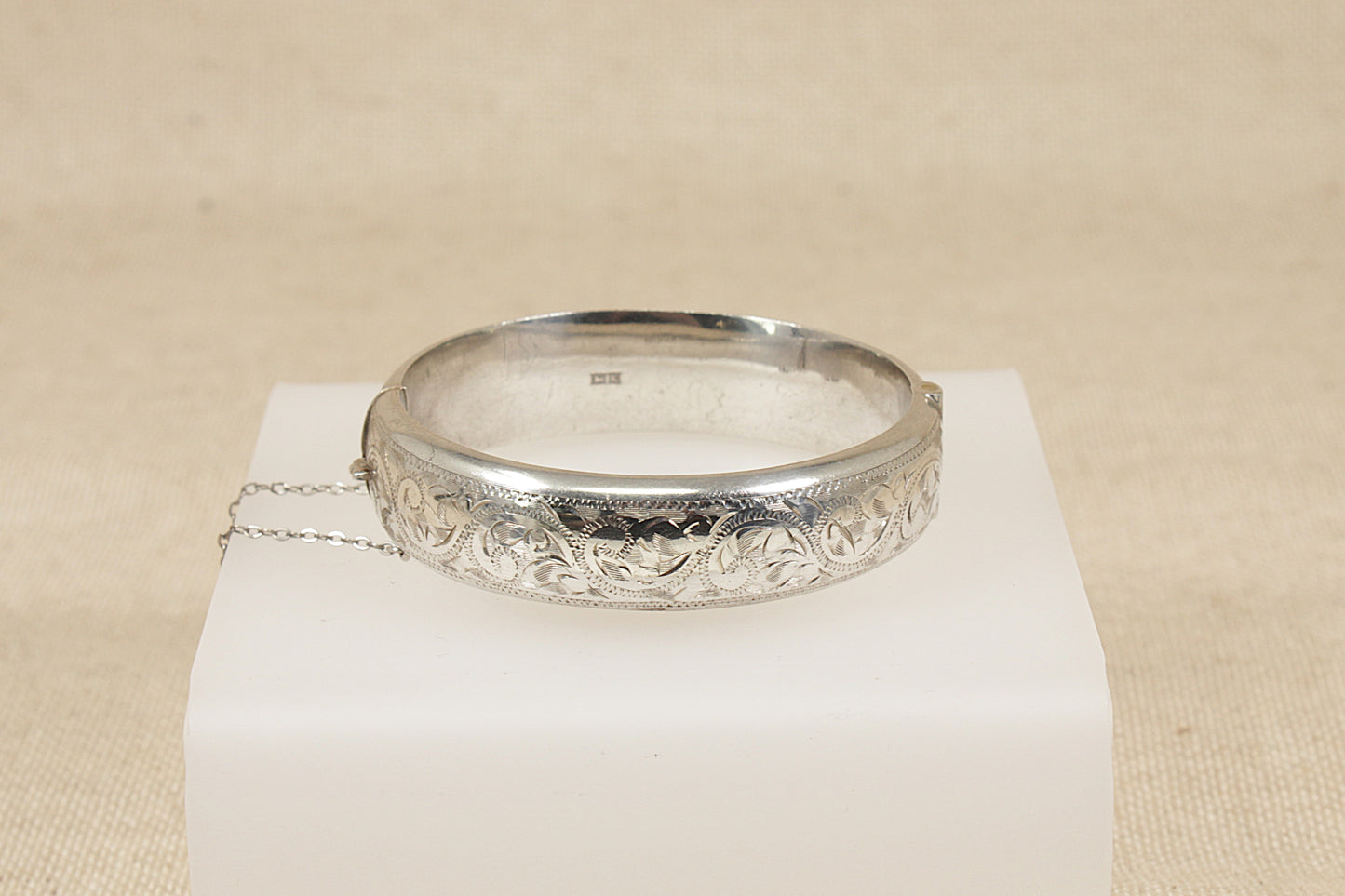 Vintage antique Silver bracelet bangle with intricate design on a white stand against a beige background