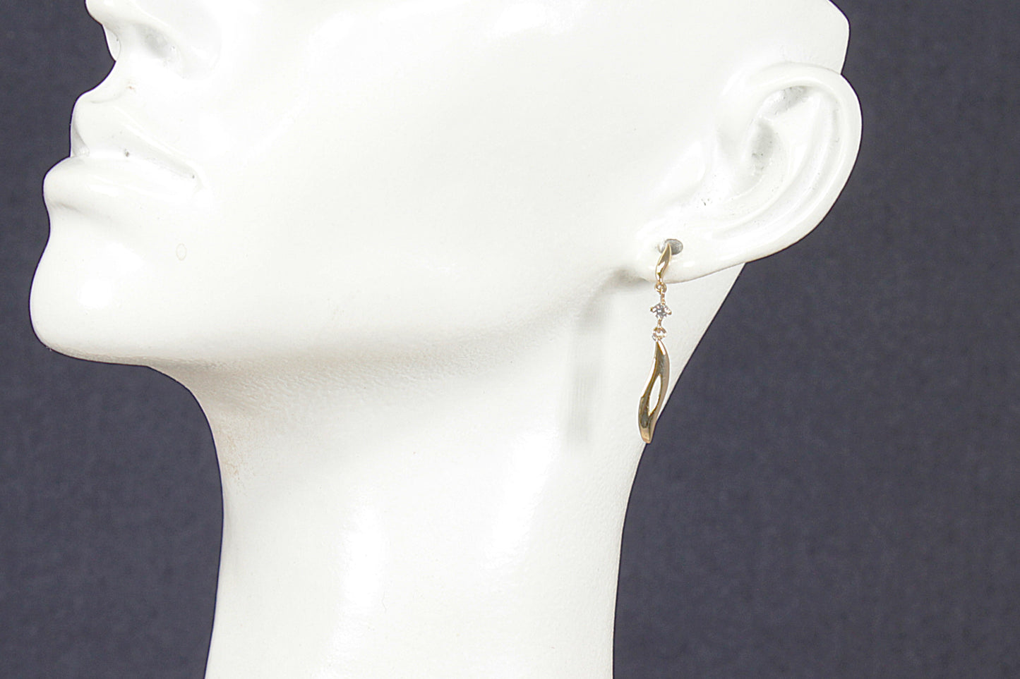 Gold and crystal earrings on a white mannequin head against a dark background