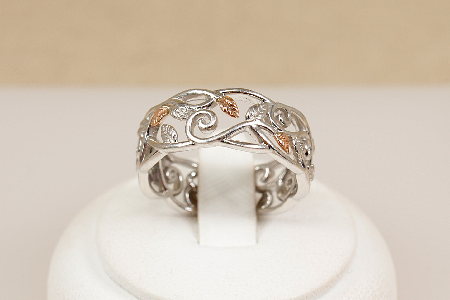 Silver ring with intricate designs on a white stand against a beige background