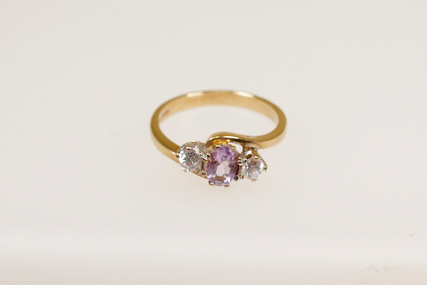 A 9ct gold ring with a central oval amethyst gemstone flanked by two single clear crystal gemstones on each side, Inside the band it has Birmingham hallmarks. UK Finger size N.