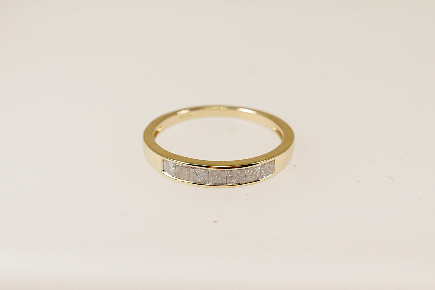 A 9ct gold band ring with channel-set princess cut diamonds around the middle section, The ring is in excellent condition and inside the band it has Birmingham hallmarks for 9ct Gold. UK Finger size O