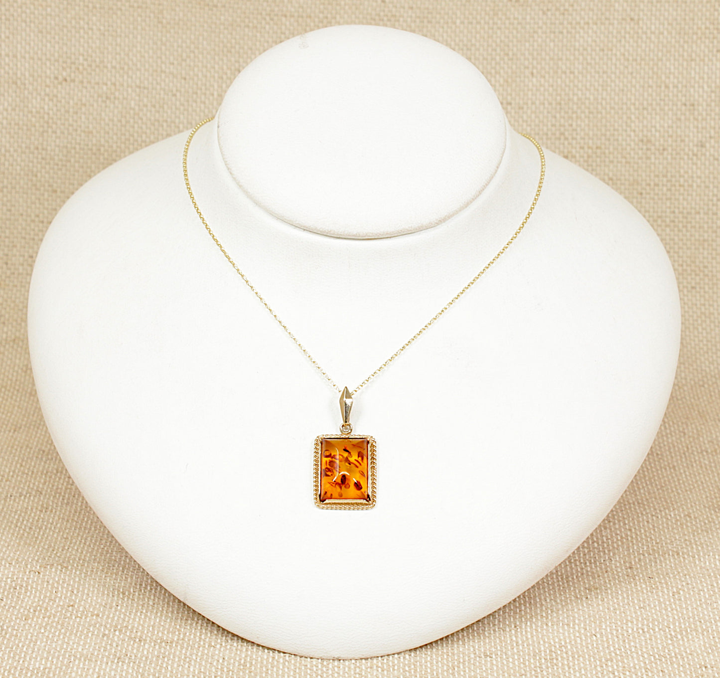 This 9ct gold rectangular amber pendant is a true vintage-inspired treasure! The cabochon cut amber, with its rich golden hues and smooth, domed shape, gives the piece a warm organic beauty. The ornate bezel setting with intricate scroll goldwork adds a touch of elegance and craftsmanship. The pendant has London Hallmarks and sits on an 18 inch 9ct Gold chain, both are in excellent condition. Pendant size: 18 x 15mm.