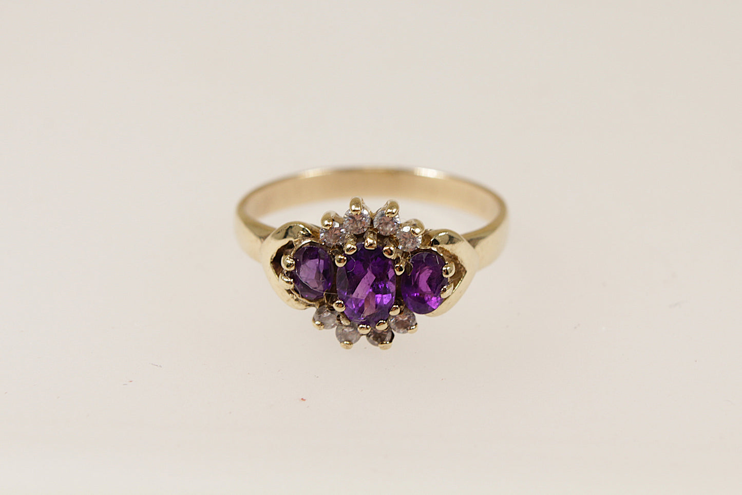 A 9ct gold ring with a floral-inspired design, featuring a central oval amethyst and surrounded by smaller amethysts and cubic zirconia gemstones. UK Finger size O.